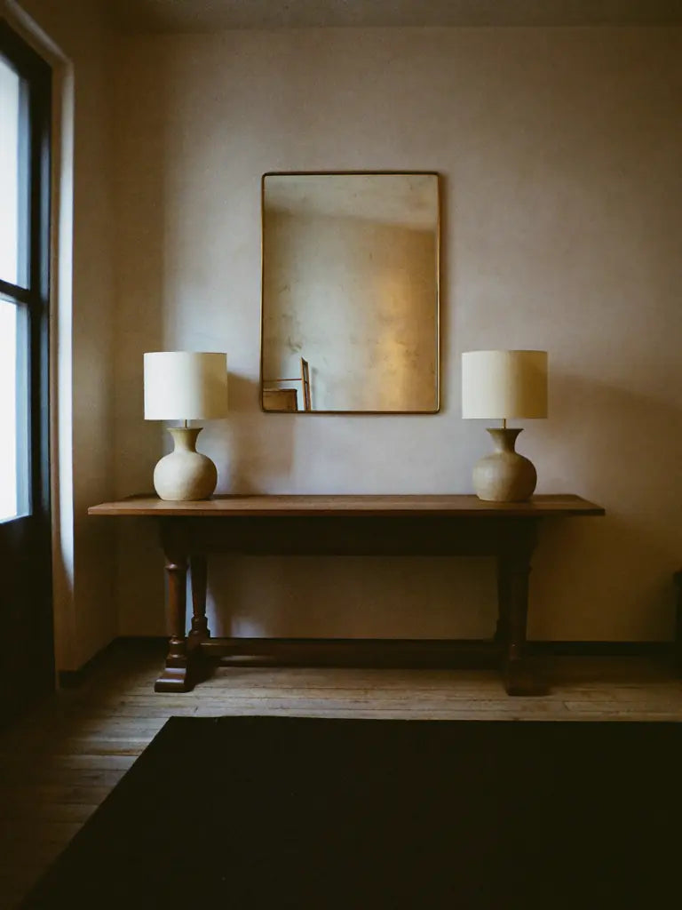 A walnut console with a pair of ceramic lamps under an antiqued mirror