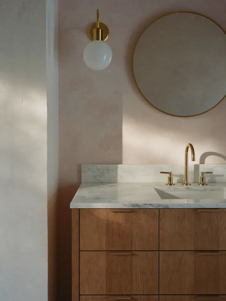 A cerused oak vanity with a marble top and a brass sconce