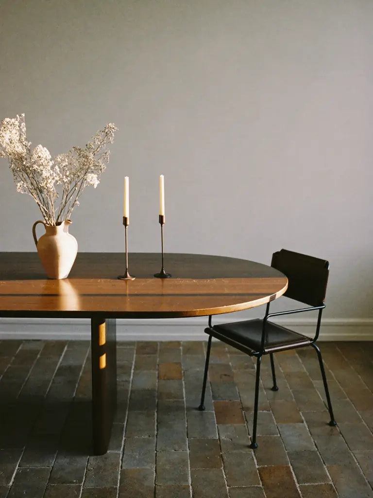 The end of a dark walnut table with iron candlesticks and a terracotta pitcher