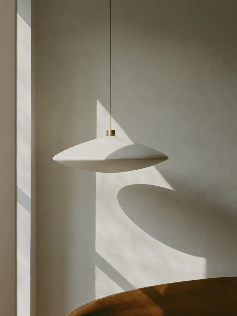 A white plaster pendant against a limewash wall with a fan of window light